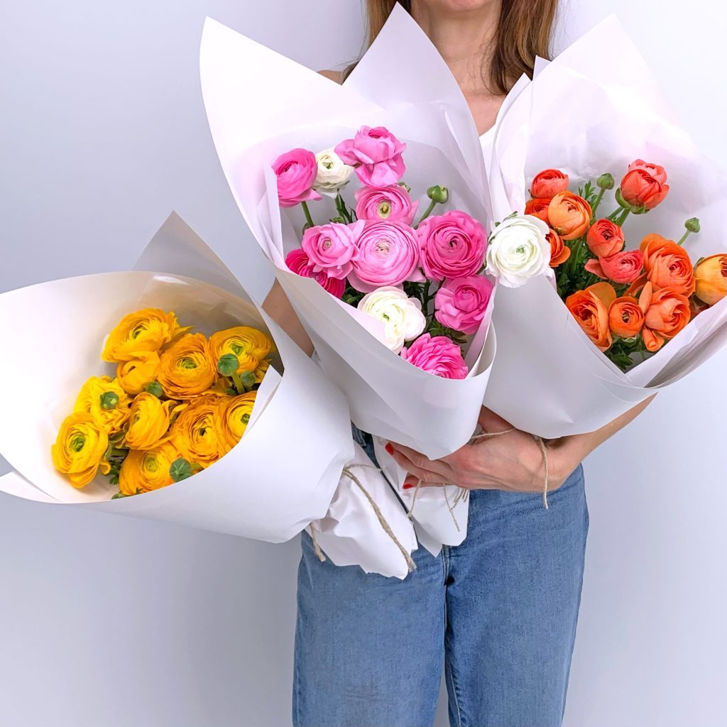 Florist holding mixed ranunculus bouquet in pink, orange and yellow tones